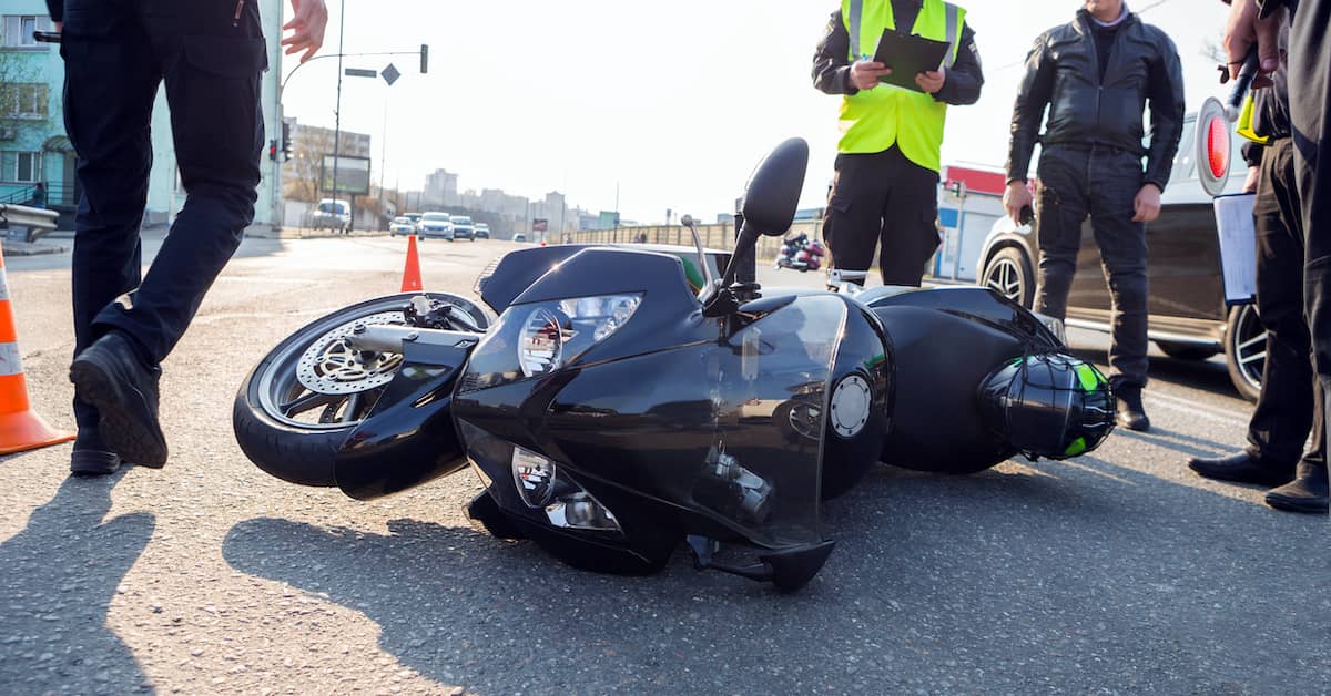 emergency personnel standing over an overturned motorcycle at the scene of a motorcycle accident