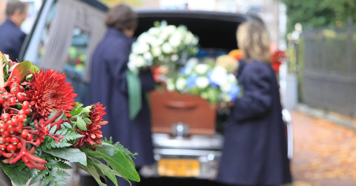 mourners standing at the back of a hearse with the casket of a deceased loved one
